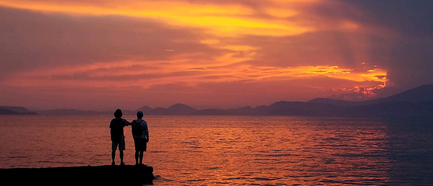 image of two people facing a sunset over a large body of water