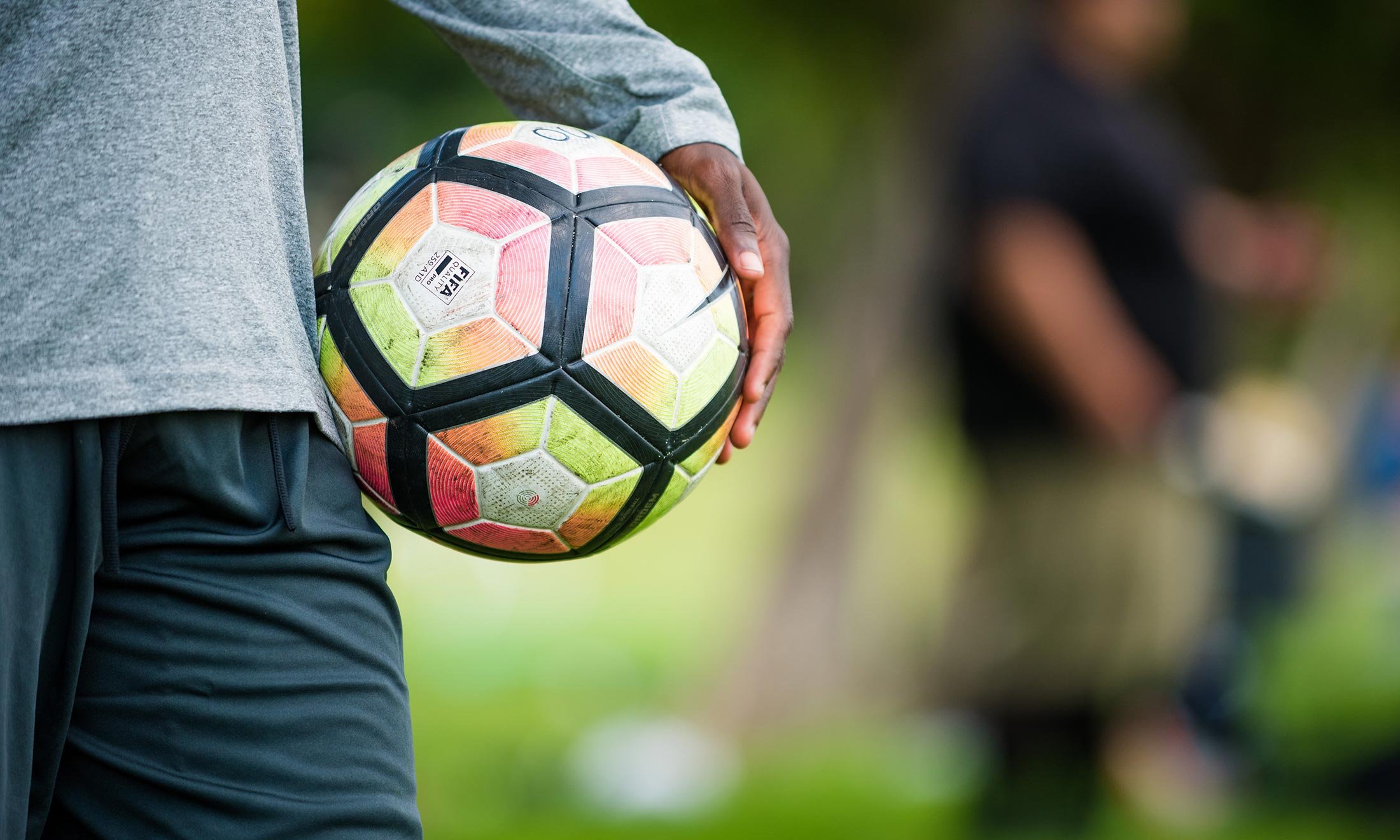 Close up of soccer player Wilfred Williams' hand holding a pink and yellow soccer ball at his side while outside during soccer practice