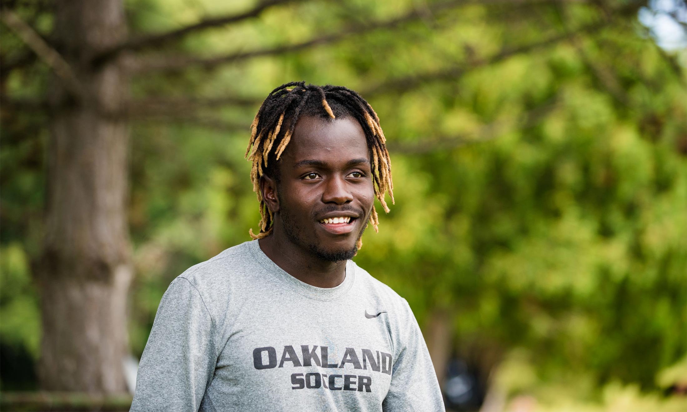 Oakland University soccer player Wilfred Williams smiles outside during practice in a gray Oakland University soccer shirt