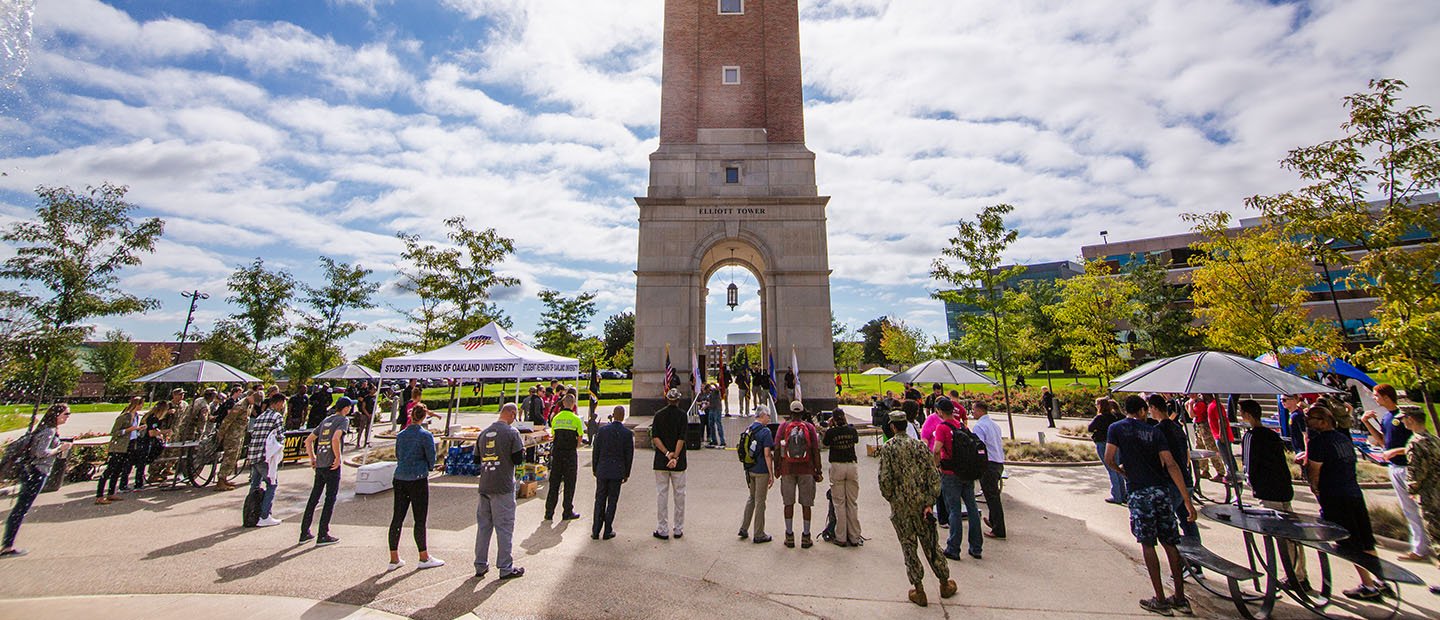 Large group of people some in military uniforms gather in front of Elliott Tower on Oakland University's campus