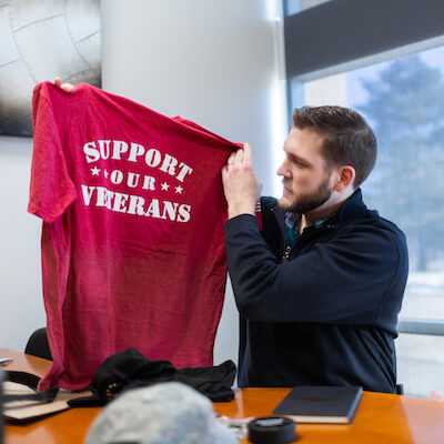 Man sitting at desk holds up tshirt that says 