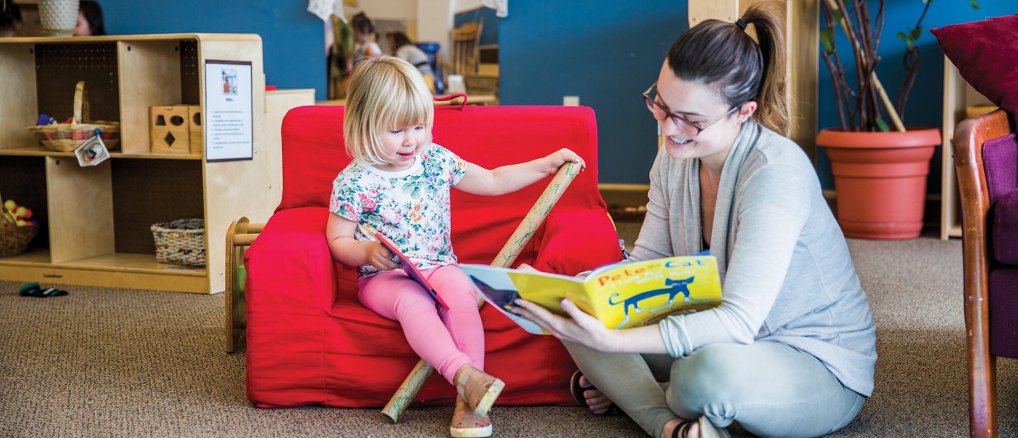 Woman reading book to child sitting on a chair