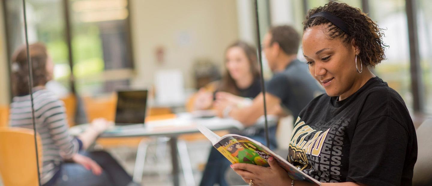 female student wearing a black Oakland University shirt, reading a book