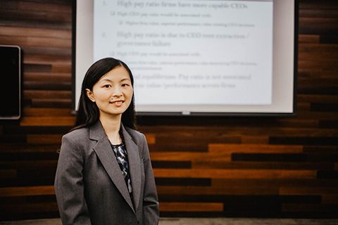 Sha Zhao standing in front of a projector screen, smiling at the camera