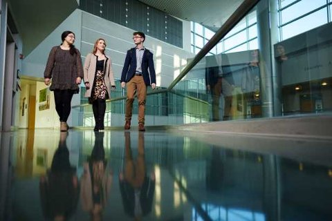 The OU Business Honors Program graduates, Alayna Gotham, Michaella Merlo, and Robert Round, walking in a building.