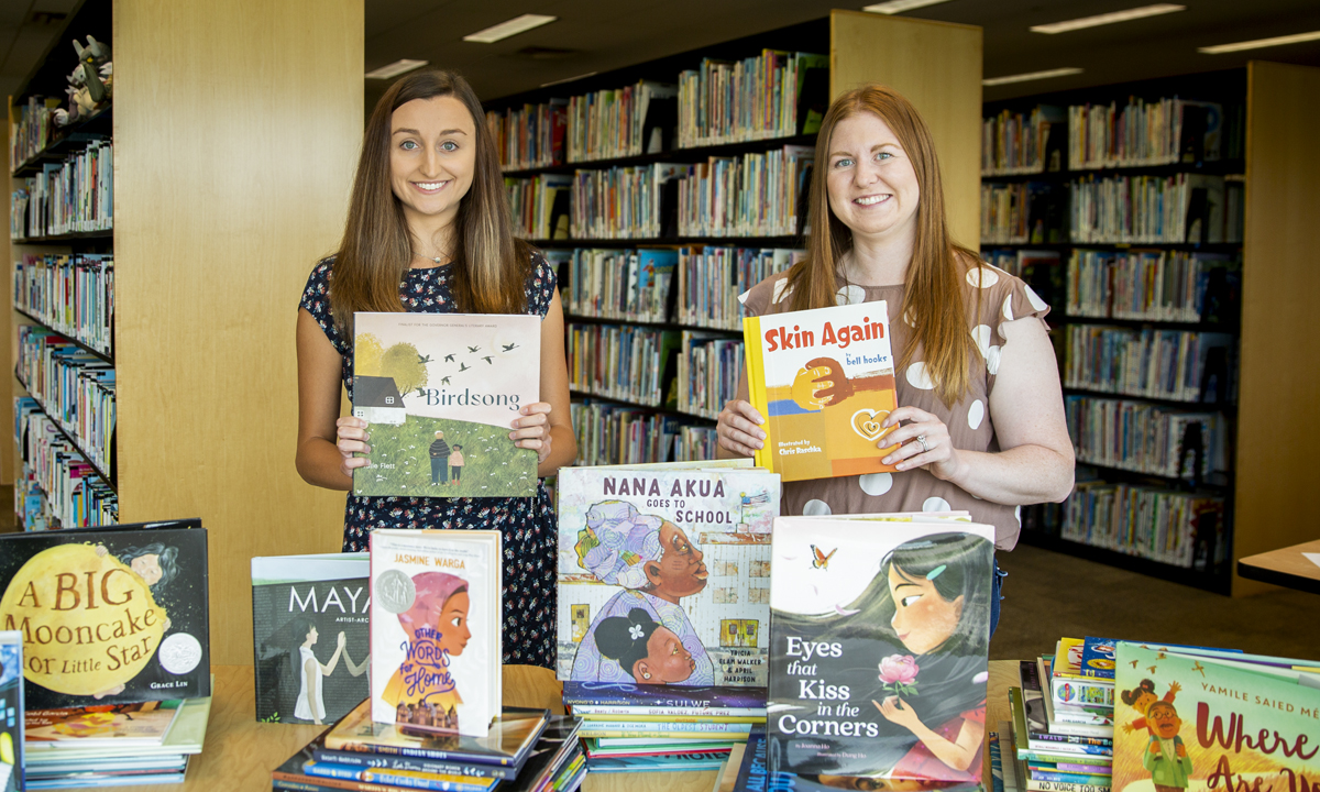 Image of two college students standing with stacks of books in a library