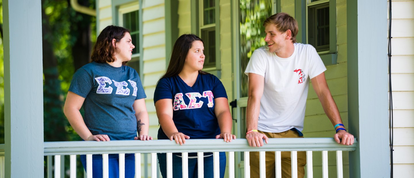 students on a porch wearing shirts with Greek letters