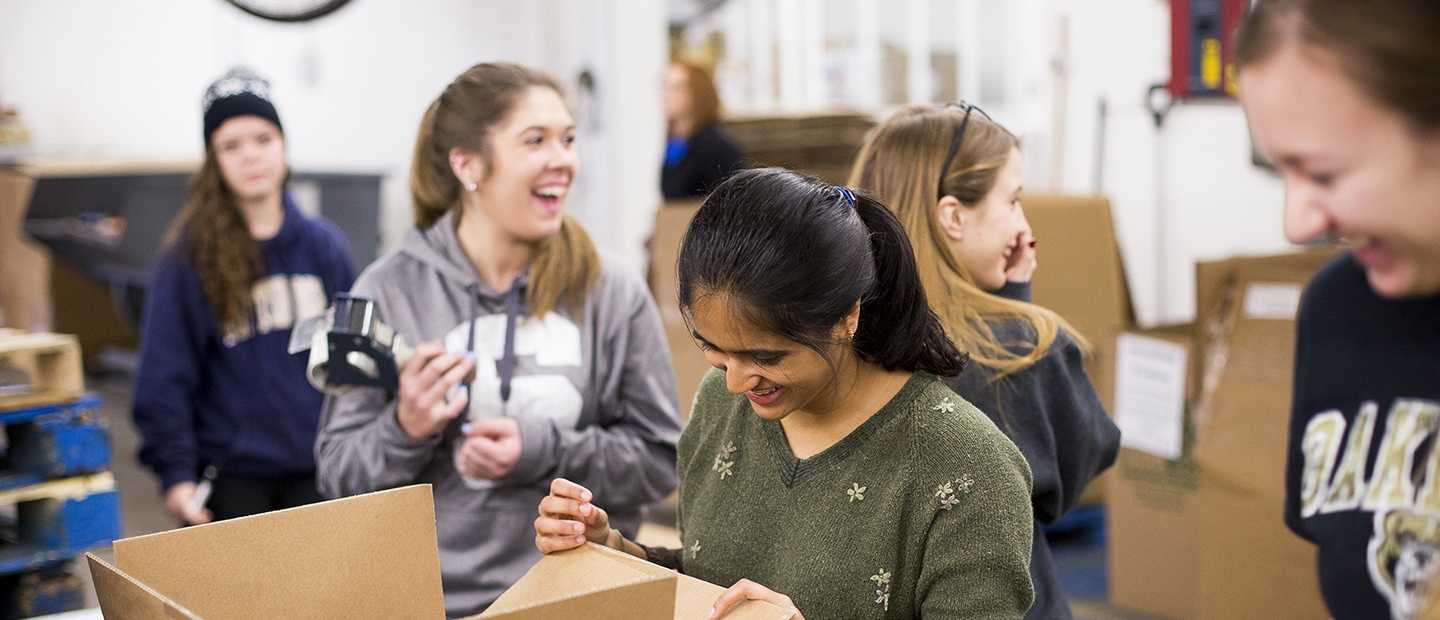 image of five women in a warehouse who are laughing and packing boxes