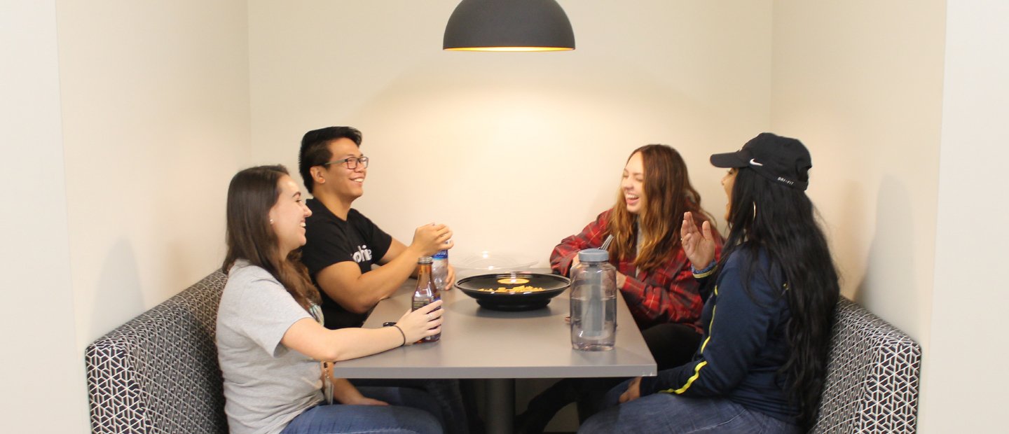 four students seated at a table with beverages and a bow of food in the middle