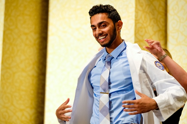 A student has help putting on his white coat on stage at the White Coat Ceremony. 
