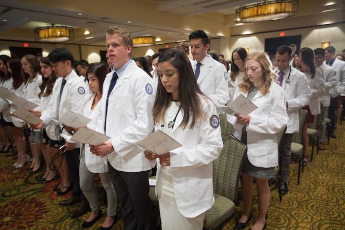 Students standing and reading programs at the White Coat Ceremony