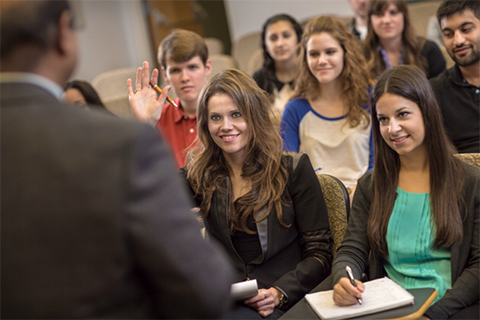 student raises her hand with professor in the foreground