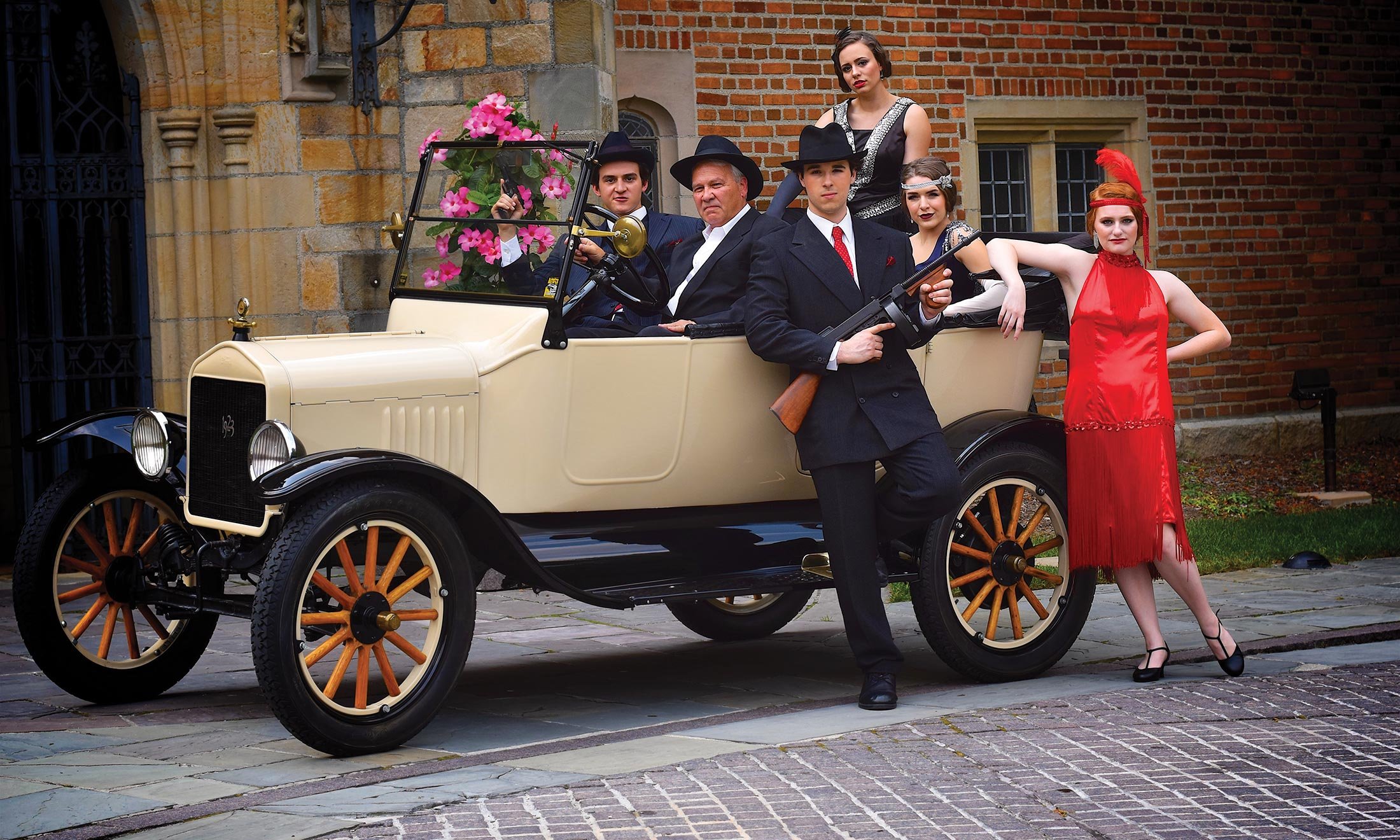 Oakland University acting majors, dressed in 1920s garb, sit inside of a vintage car in front of Meadow Brook Hall 