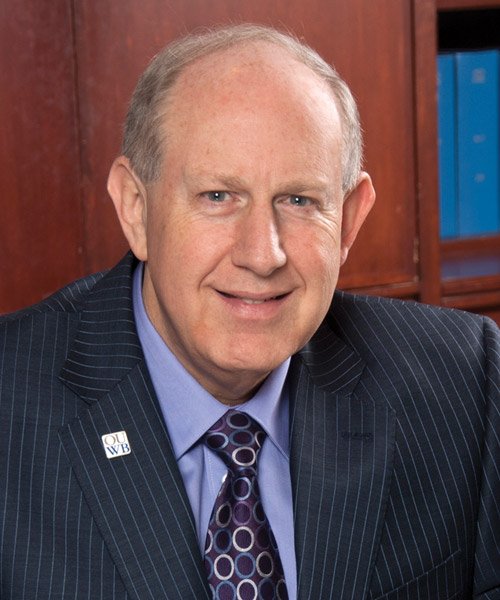 Head shot of Dr. Jeffrey M. Devries. Wearing a navy blue pin striped suit with an O U W B logo pin on the lapel. Appears to be sitting in front of a wooden file cabinet.