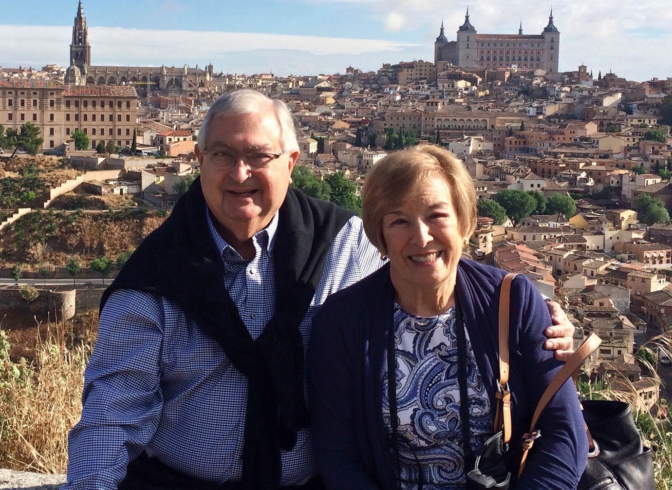 Walter and Donna Young stand smiling in front of European city with cathedrals in the background