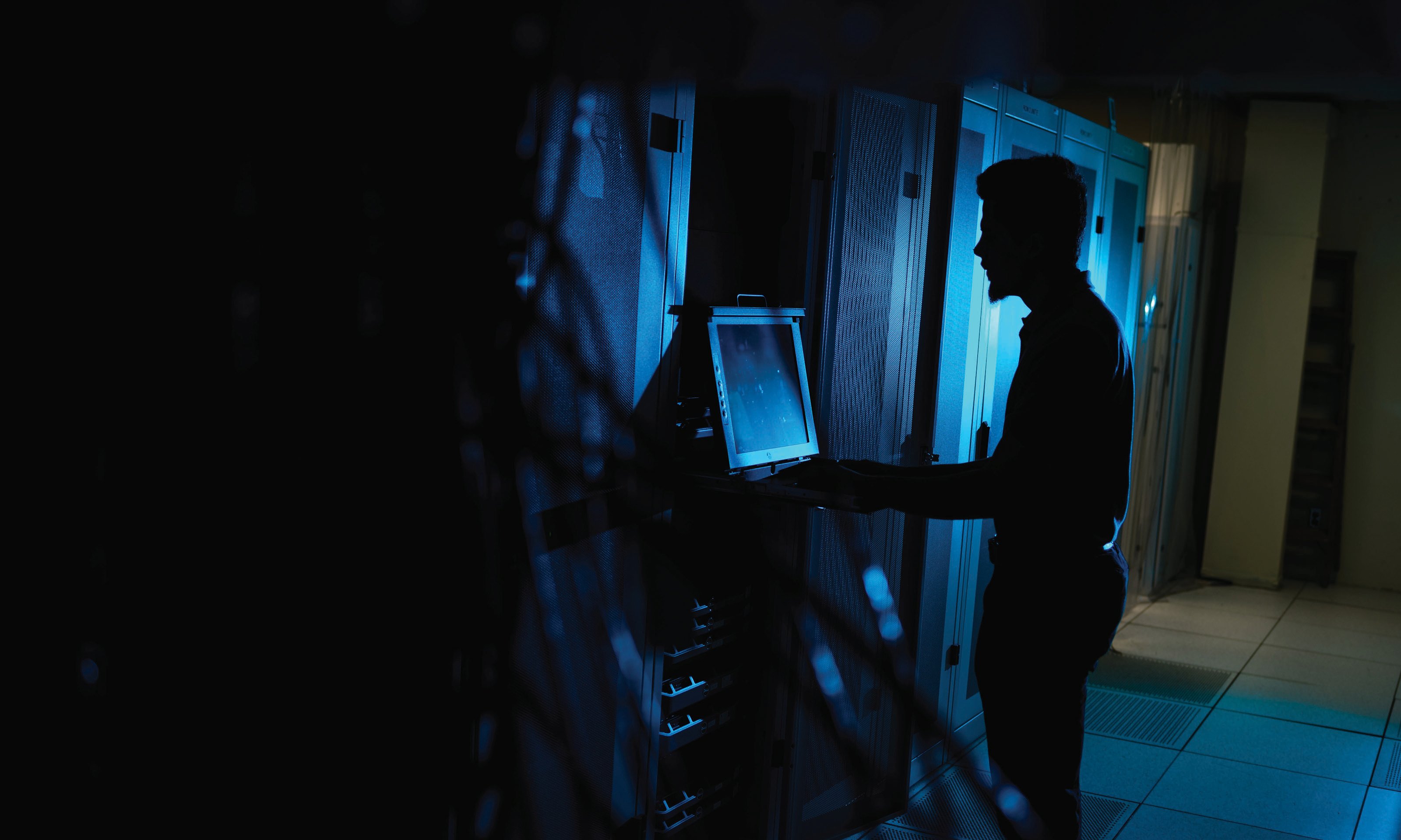 silhouette of a man standing at a computer in a dark room