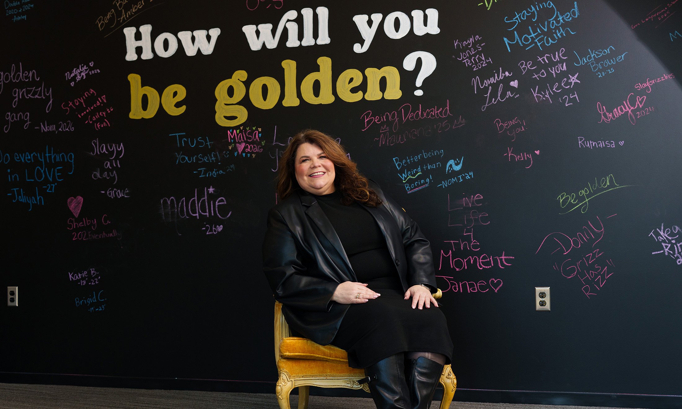 A woman in the gold seat in front of a chalkboard that says "How will you be golden?"