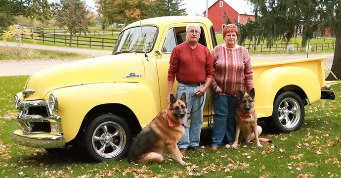 Two people and a dog standing in front of a truck