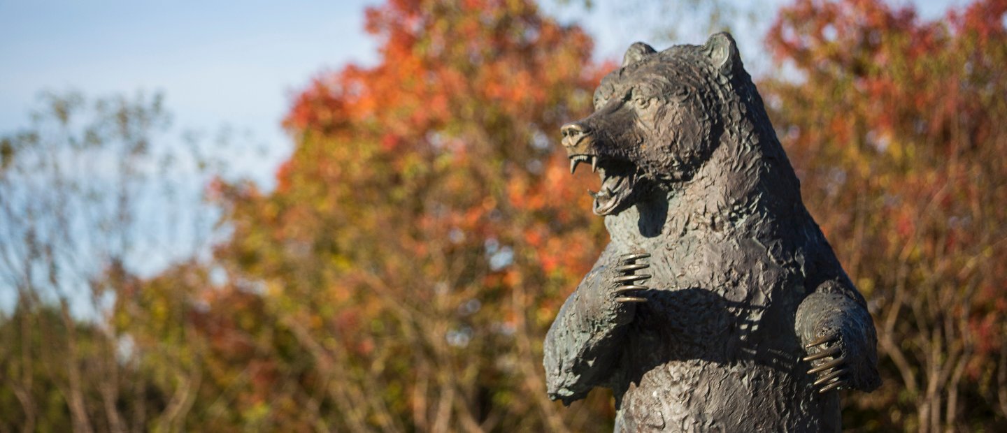 The Grizz bear statue in front of trees with red and green leaves.