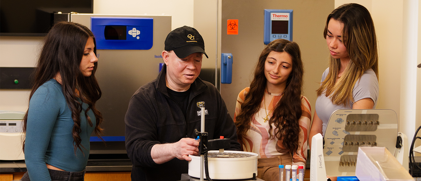 Three women observing an instructor working in a lab.