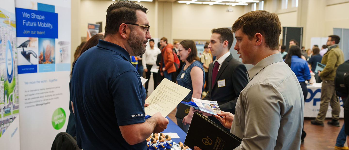 Employer talking with and reviewing the resume for a male student at a career fair.