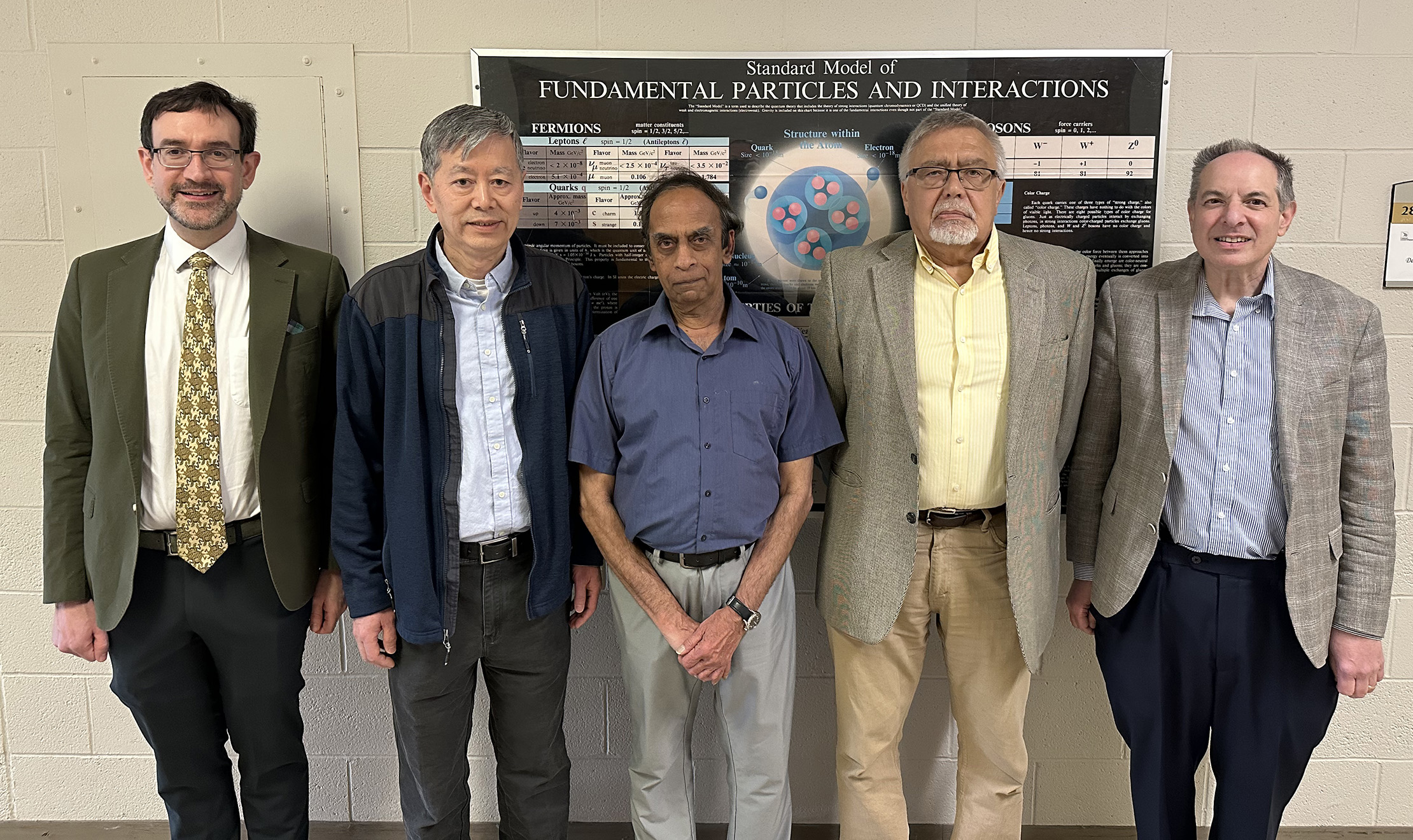 Oakland University Physics professors Ilias Cholis, Yang Xia, Gopalan Srinivasan, Andrei Slavin and David Garfinkle pose for a photo in front of a Physics poster.