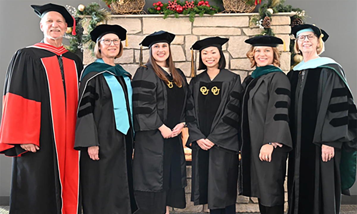 Group of people standing smiling at camera with graduation gowns on.