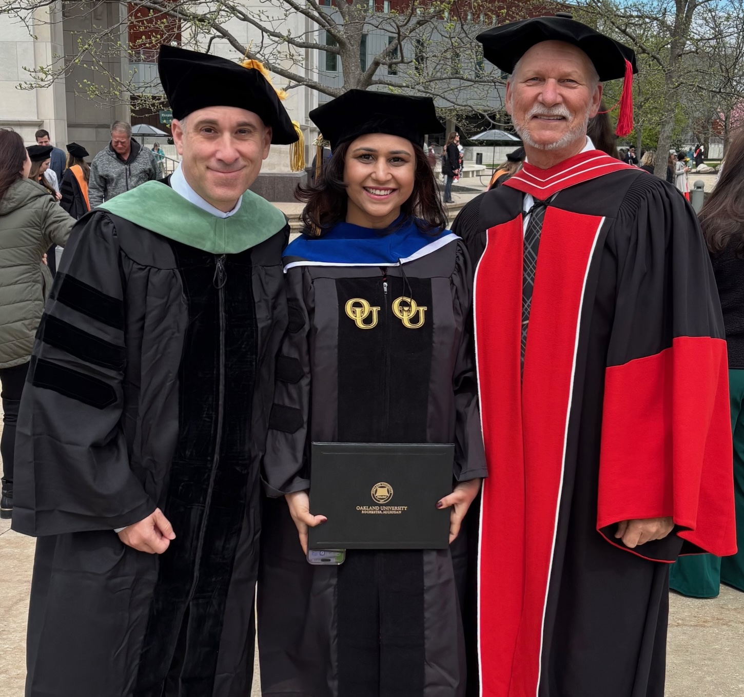 three people in graduation gowns smiling at the camera