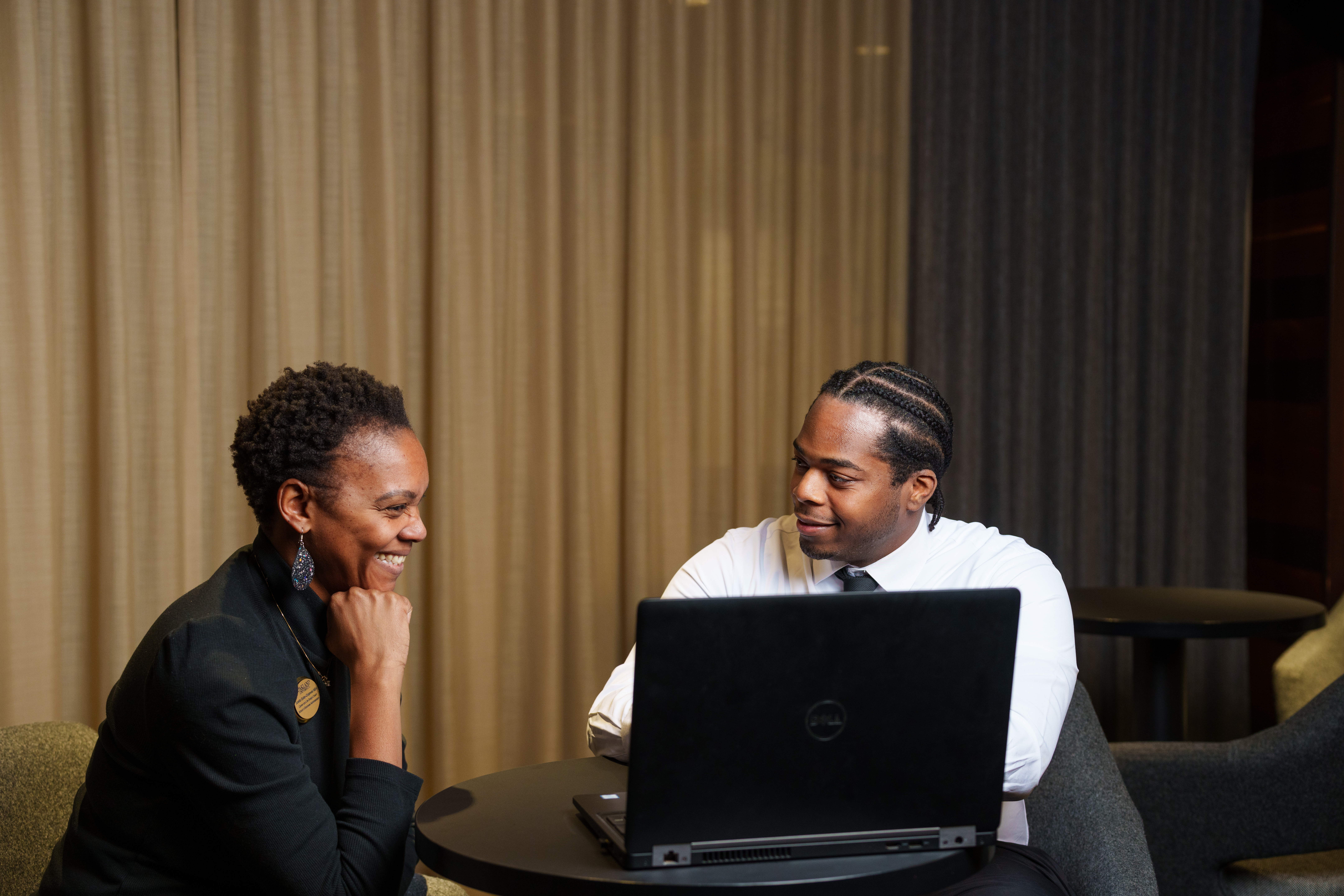 Student and staff sitting, talking and looking at laptop
