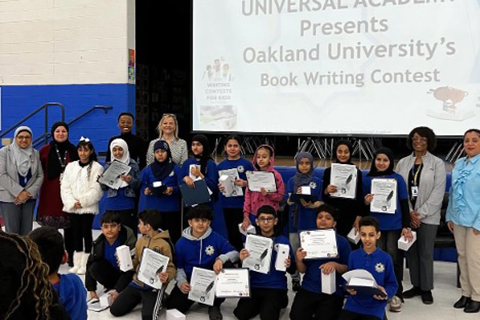 Winners of the book writing contest posing with awards on stage.