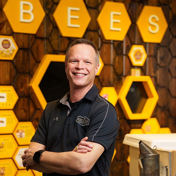 A man posing with decorative honeycombs behind him with a sign that reads 