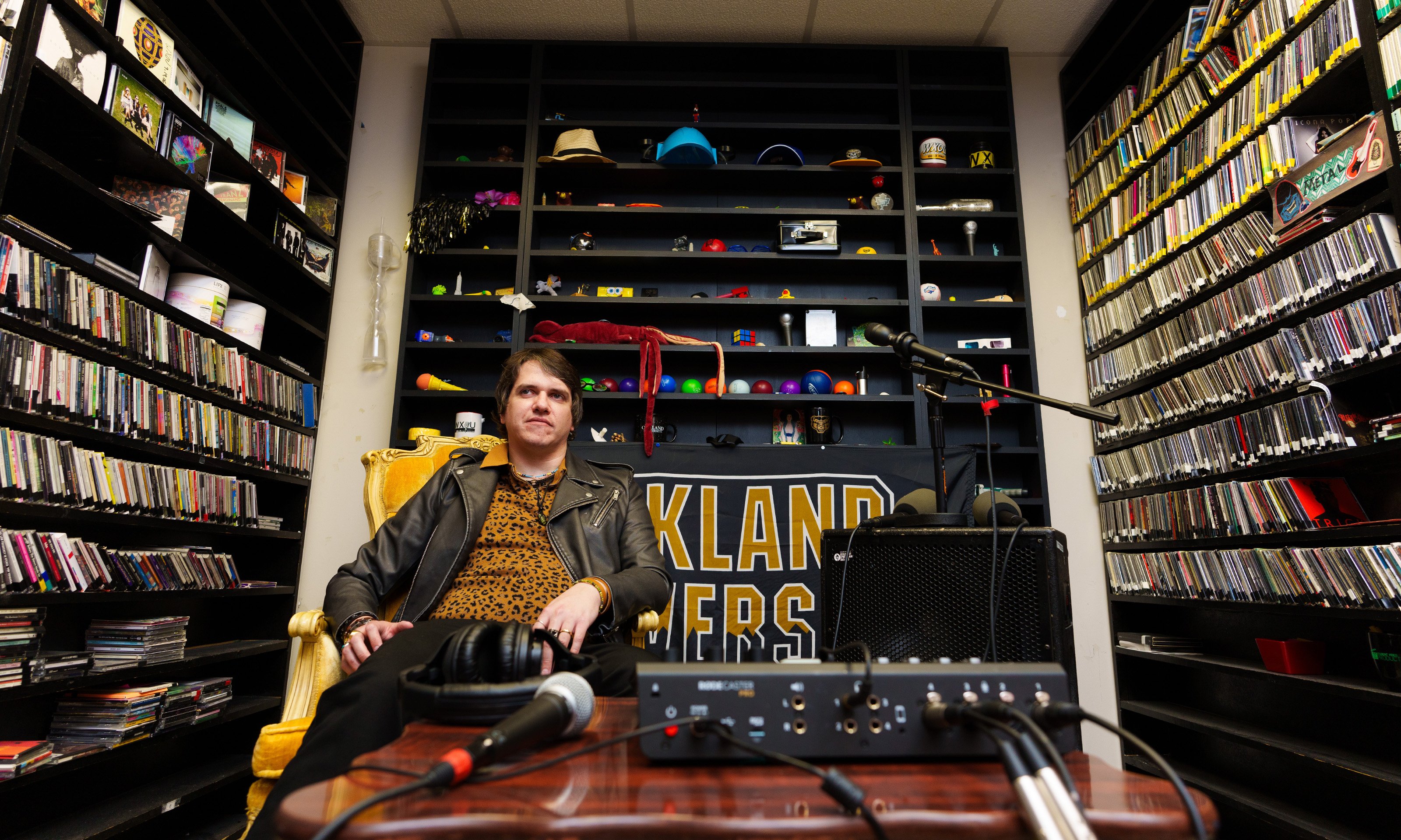 A man sitting in a gold seat surrounded by bookshelves of cds