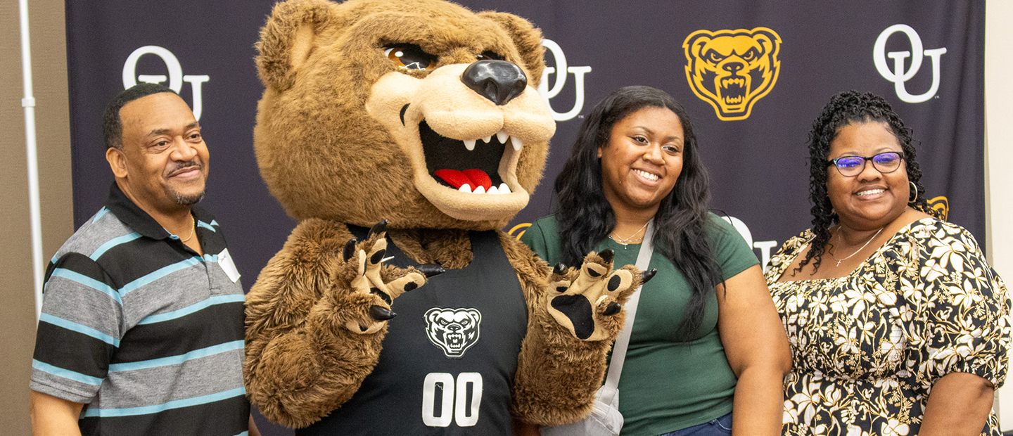 A new Oakland University student and her parents posing with the Grizz mascot